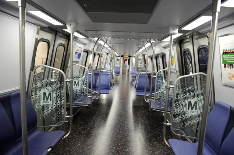 Interior view of a nearly empty Washington DC Metro train, featuring blue seats and modern design elements, celebrating the system's 50th anniversary. The focus is on the sleek, clean ambiance with illuminated signage and metallic finishes.