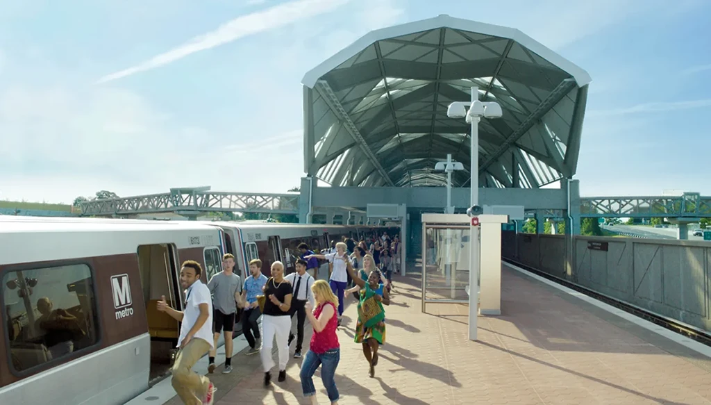A bustling Metro station features a modern architectural design with a large canopy. Passengers are disembarking from a Metro train, filling the platform with a diverse crowd. The scene captures the energy of commuting, symbolizing the 50th anniversary of the Metro system in the Washington DC region.