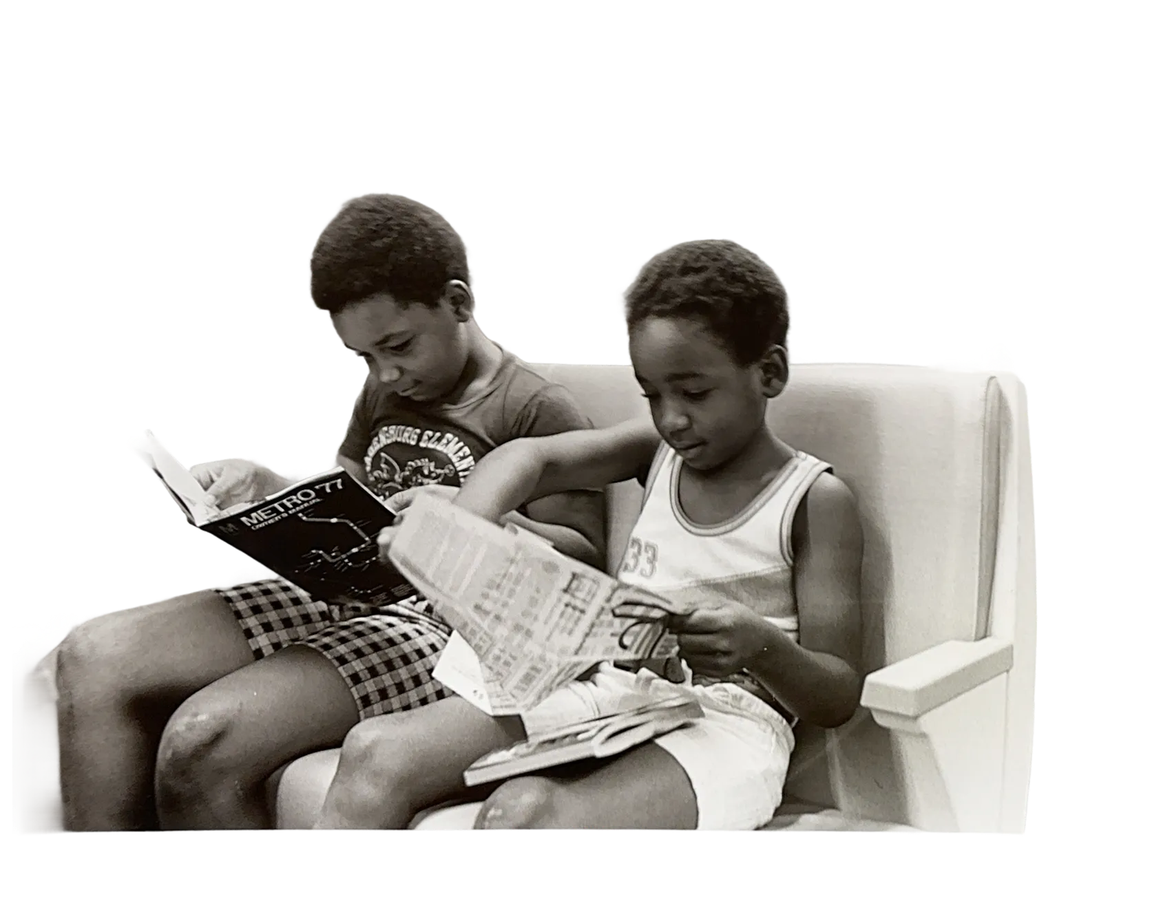 Two boys sitting on a bench, engrossed in reading magazines related to the Metro system, capturing a moment of curiosity and engagement. One boy wears a tank top and shorts, while the other is in similar casual attire, both focused on their reading material.