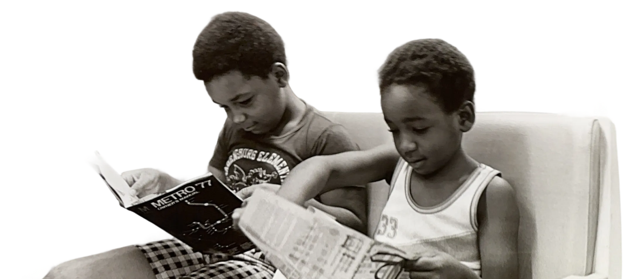 Two young boys sit side by side on a bench, focused on reading magazines. One boy in a black shirt reads "Metro 77," while the other in a white tank top examines a newspaper. Their concentration and relaxed posture highlight a moment of exploration and engagement, reflecting life in the Washington DC Metro area.