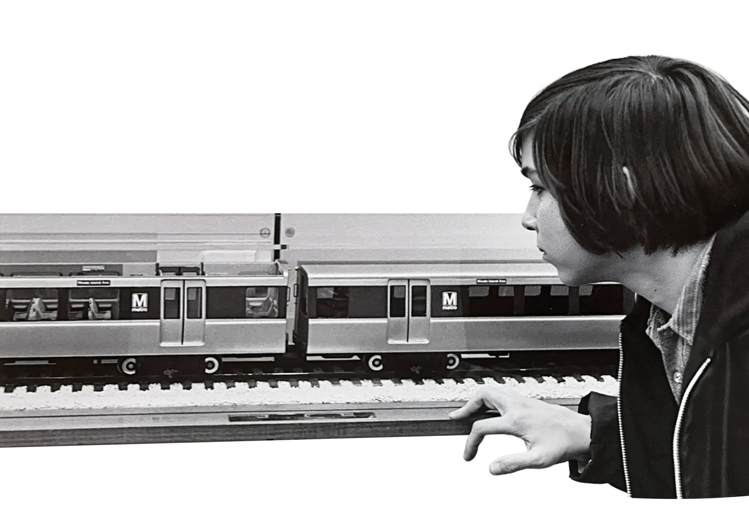 A young person curiously examines a model train set representing the Washington DC Metro system, highlighting its design and detail. The scene captures the excitement of the Metro's early days in black and white, emphasizing its significance in the region's history.