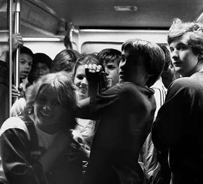 A group of young people packed together in a subway car, showing expressions of excitement and curiosity, celebrating the vibrant history of the Washington DC Metro system. The image captures a moment of commuting life, reflecting the social atmosphere within the transit system over the years.