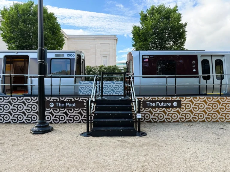 A display featuring two Metro trains on a platform with a decorative mural below that reads "The Past" and "The Future," celebrating the 50th anniversary of the Washington DC Metro system. The scene includes trees and a cloudy sky in the background.
